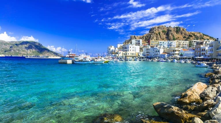 Il porto di Pigadia a Karpathos con barche ormeggiate e acque turchesi, ideale per una vacanza last minute in Grecia.