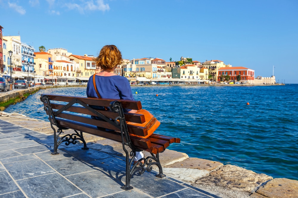 La Canea Giovane donna seduta sulla panchina e guardando il vecchio porto di Chania, Creta, Grecia