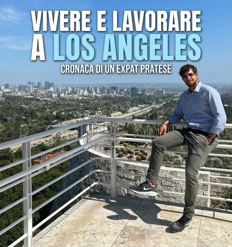 Un uomo sorridente seduto su una ringhiera panoramica con lo skyline di Los Angeles sullo sfondo e la scritta Vivere e Lavorare a Los Angeles.